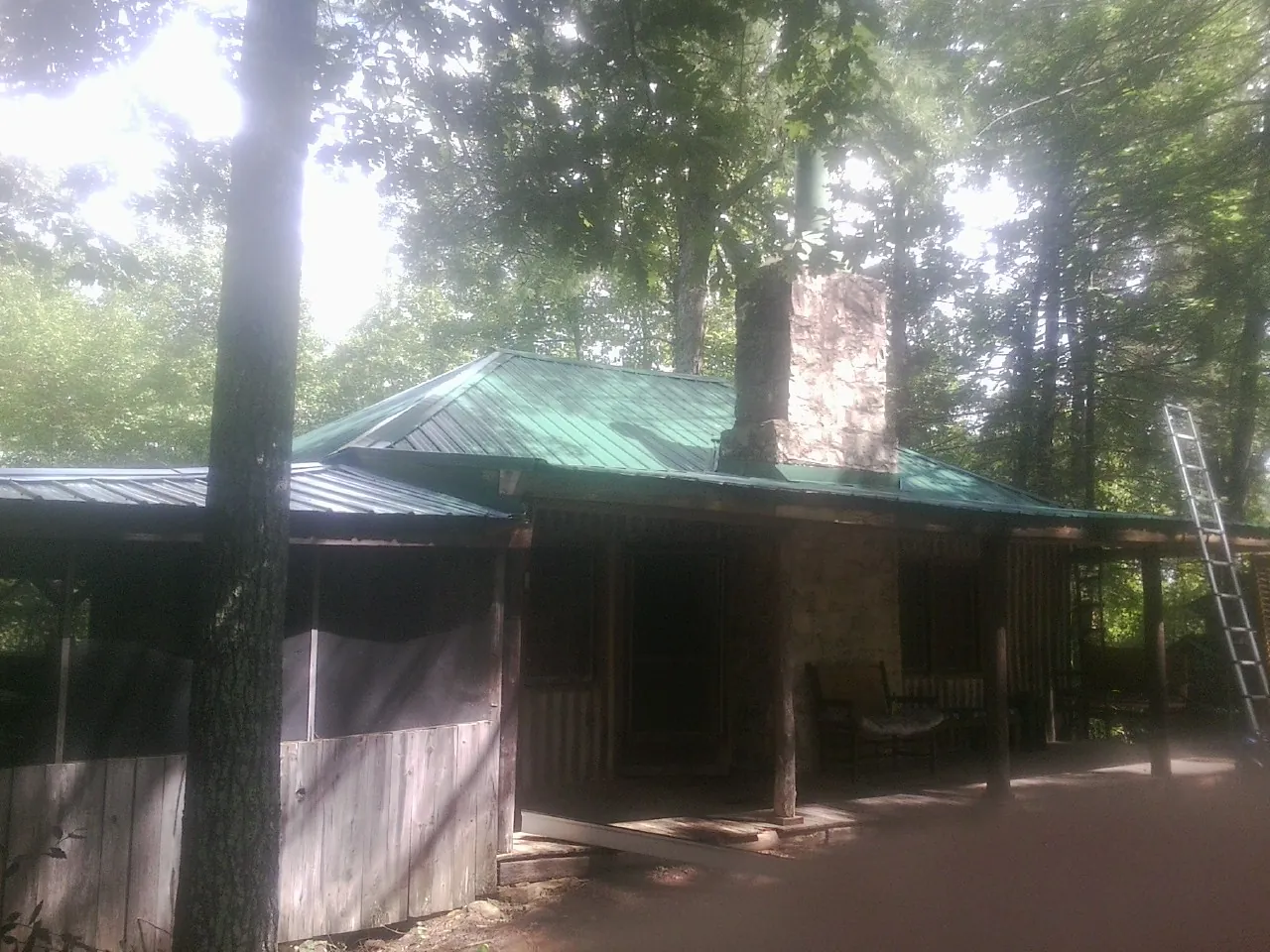 Green metal roof and stone chimney above a log cabin porch in Windsor